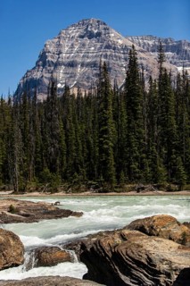 Majestic mountains behind a flowing river with rocky foreground inside Yoho National Park, in
