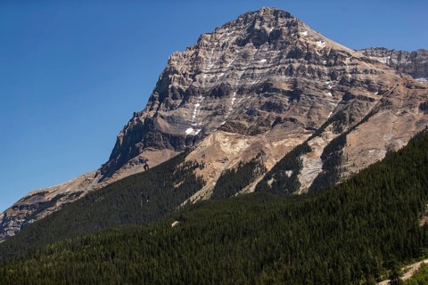 Dramatic mountain peak rising above a dense green forest as viewed from the Trans Canada Highway in