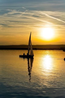 Lake Neusiedl, Burgenland, Austria, Europe, Sailboat gliding on calm water in the golden glow of