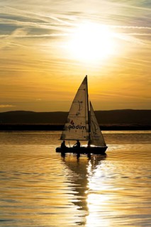 Lake Neusiedl, Burgenland, Austria, Europe, Sailboat at sunset with reflection on calm water under