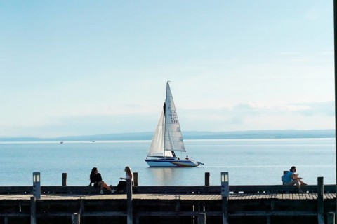Lake Neusiedl, Burgenland, Austria, Europe, A sailboat sails calmly on a lake while people relax on