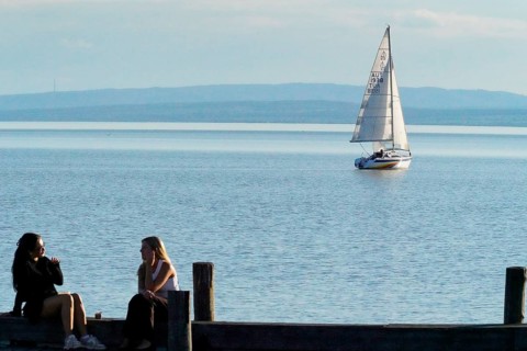 Lake Neusiedl, Burgenland, Austria, Europe, Two woman sit on the jetty while a sailing boat passes