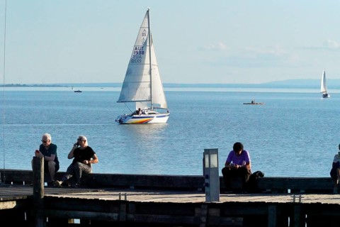 Lake Neusiedl, Burgenland, Austria, Europe, People sitting at the jetty and watching a sailing boat