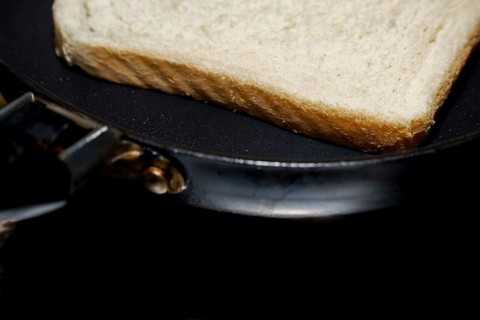 Close-up of a single slice of white bread toasting in a frying pan, suggesting a simple breakfast