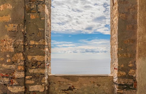 Sunny mediterranean sea scenery seen through a window opening in a historic wall seen in Liguria,