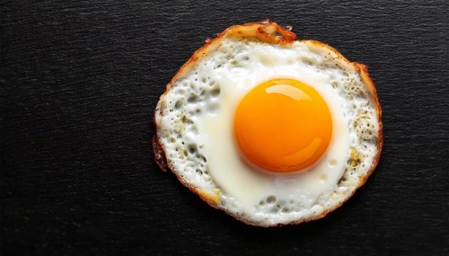 AI generated image showing a fried egg sunny side up on dark ground seen from above