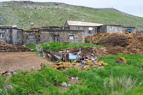 Stone house in a rural area surrounded by green hills and rocks, cow dung in front, Ardenis, Shirak