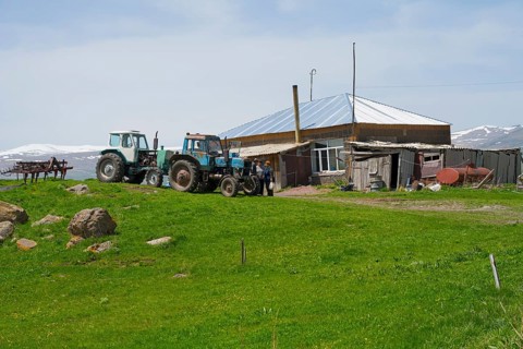 Two tractors standing on a green field next to a farmhouse and a barn, Zorakert, Lake Arpi, Shirak