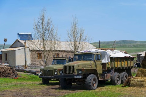 Large lorries parked on a farm in front of a stone building surrounded by green countryside, Gaz 53