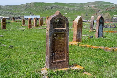 A well-preserved old gravestone on green grass in front of a hilly landscape with several
