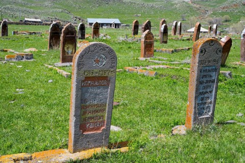 Close-up of two gravestones in a grassy cemetery with rolling hills in the background, old