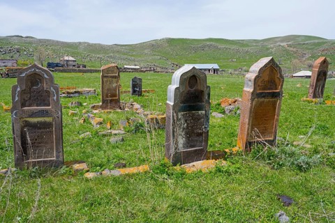 Cemetery with old weathered gravestones on green grassland with rolling hills in the background,