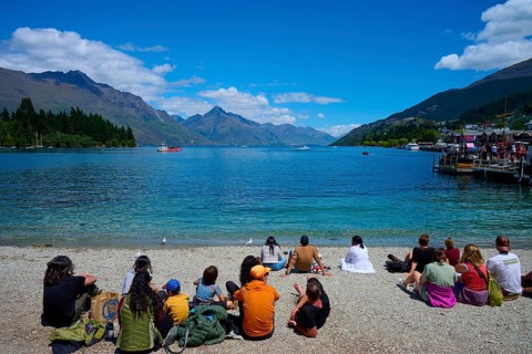 Groups of people sitting on the beach enjoying the view of the lake and mountains, Queenstown,
