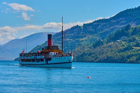 Large ship sailing across a wide lake with picturesque mountain ranges in the background,