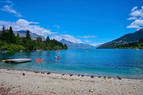 Waters with floating ducks and boats against a picturesque mountain backdrop and clear skies,