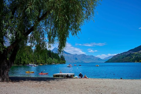 Sunny day at the lake with calm water, people relaxing on the shore and boats floating on the