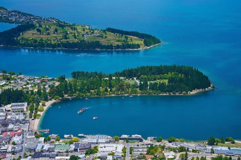 Aerial view of an urban landscape with a blue-green lake and forested peninsulas, Queenstown,