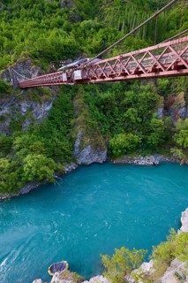Red suspension bridge over river with steep wooded cliffs and calm waters, Kawarau Gorge Suspension
