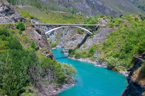 A bridge spans a turquoise-coloured river in a green and rocky landscape, Kawarau River,