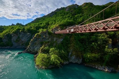 Red suspension bridge with view over the turquoise river and green surroundings, Kawarau Gorge