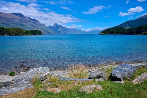 Tranquil seascape with grassy rocks and mountains in the background, Queenstown, Queenstown-Lakes