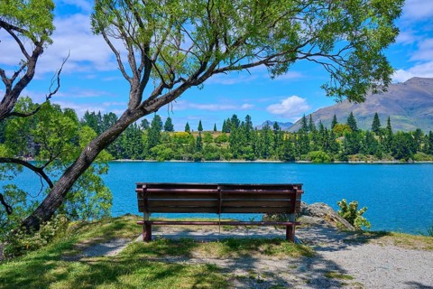 Idyllic landscape with bench and view of a lake and mountains in the background, Queenstown,