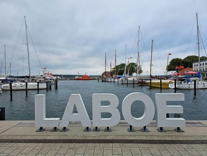 Harbour with large LABOE lettering in the foreground, surrounded by boats and a cloudy sky, Laboe,