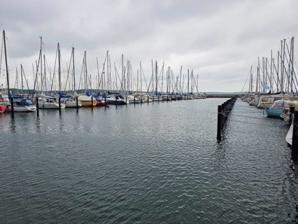 Numerous moored sailing boats in the harbour with cloudy sky, calm sea and parallel jetties, Laboe,
