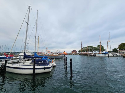Sailboats and yachts in the harbour under a grey sky, surrounded by water and harbour structures,