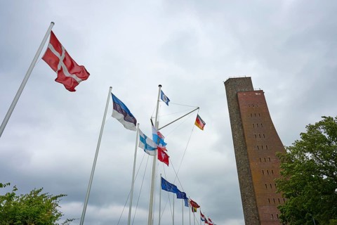 National flags next to a high brick tower under a cloudy sky, Naval Memorial, Laboe, Kiel Fjord,