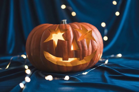 Carved Halloween pumpkin with star eyes glowing on black fabric with festive lights. Generative AI,