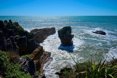 Dramatic rocks rise from the ocean waves, surrounded by natural wilderness, Pancake Rocks,