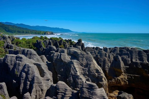 Striking rock formations tower over the roaring sea under a clear blue sky, Pancake Rocks,