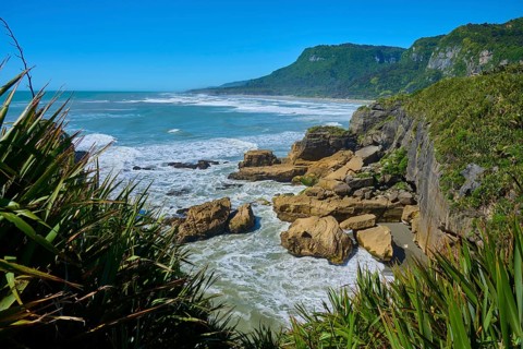 Stormy coastline with rocks and lush vegetation under a blue sky, Pancake Rocks, Westport,