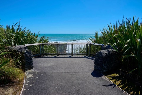 Plants flanking a platform overlooking the sea, framed by a clear blue sky, Pancake Rocks,