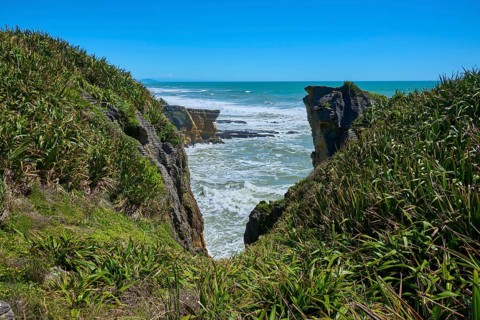 Cliff landscape with lush green vegetation and roaring sea behind the rocks, Pancake Rocks,