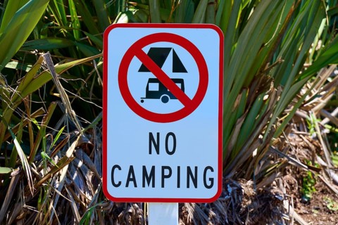 Prohibition sign for camping in a natural environment with green plants, West Coast, South Island,