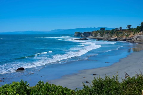 A peaceful coastal landscape with blue waves crashing against sand and cliffs under a clear blue