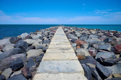 A stony path leads into the sea, surrounded by a sunny coastal landscape, Mana Bay, Patea,