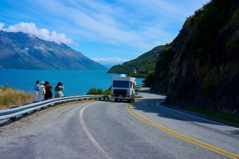 People enjoying travelling and a motorhome on a winding road next to a lake surrounded by