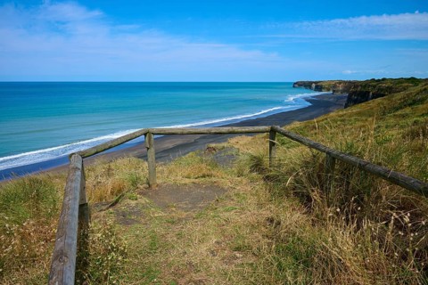 Viewing platform with wooden railing overlooks black sand beach and cliffs on a quiet coast, Mana