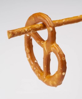 Small lye pretzel hanging on a salt stick in light back