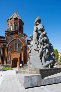A stone monument in front of a church with classical architecture under a clear sky, Church of the