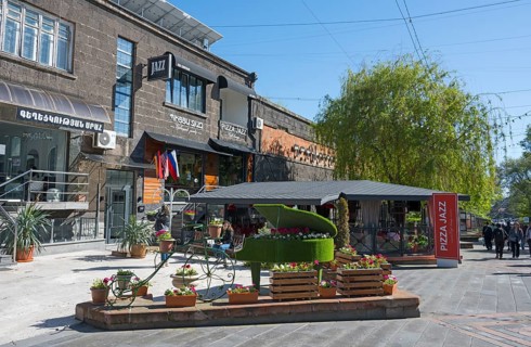 Lively street scene with a decorated piano, flowering plants and pretty buildings on a sunny day,