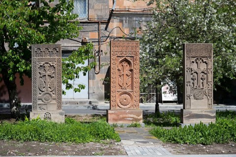 Three artistically engraved khachkars stand in a green setting, cross stones, khachkars, Gyumri,