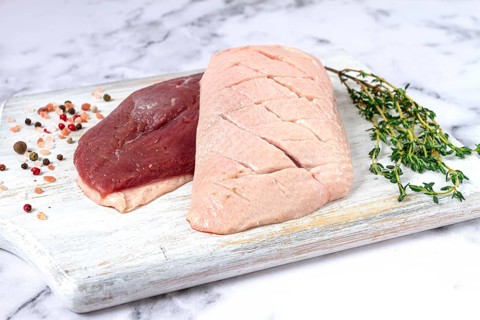 Fresh raw duck breasts, spread on a wooden cutting board, with herbs and spices, on a white marble