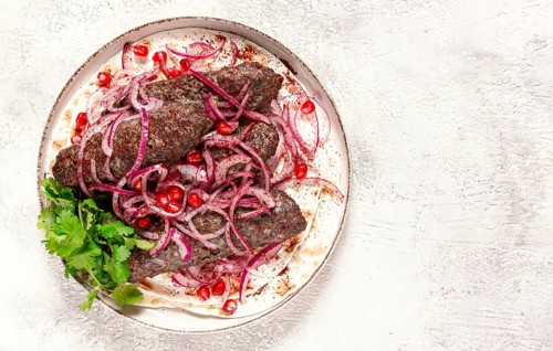 Grilled kebabs topped with onions and pomegranate on a white plate in a bright kitchen setting