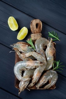 Fresh raw, white-footed shrimp, tiger prawns vannamei, on a wooden cutting board, with lime slices,