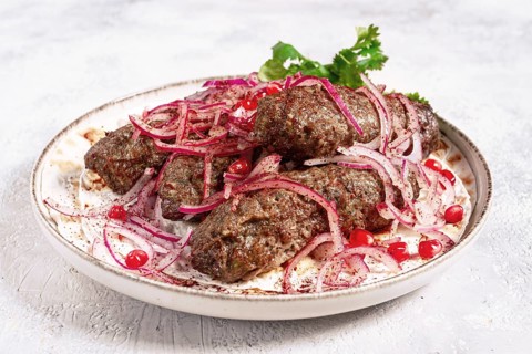 Grilled kebabs topped with onions and pomegranate on a white plate in a bright kitchen setting