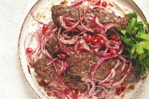 Grilled kebabs topped with onions and pomegranate on a white plate in a bright kitchen setting